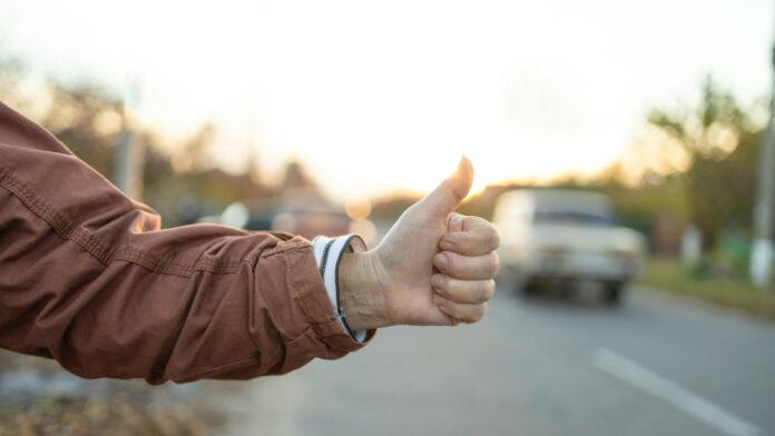 Female hand and hitchhiking sign on road, traveling by autostop in the city Woman try stop car thumb up Adventure and tourism concept