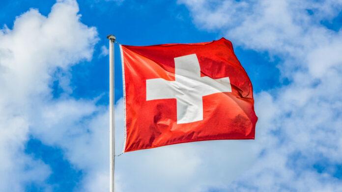 Swiss flag waving in the wind on a sunny day with blue sky and clouds