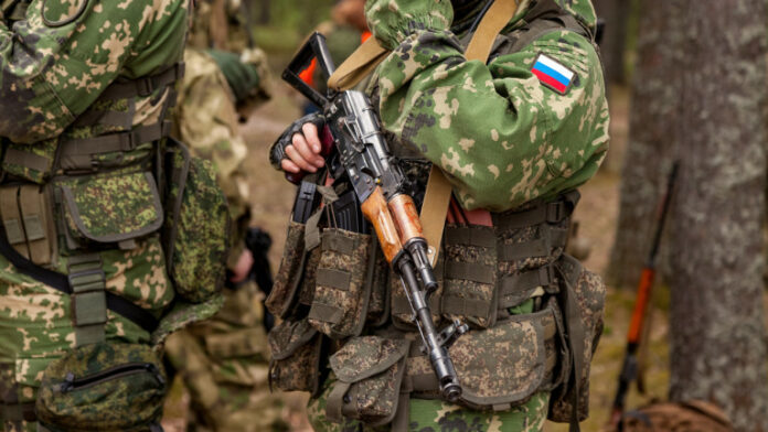 Close up hands russian soldier man dressed military camouflage uniform holds weapon in woodland at soldiers background Male border guard in country border holding machine gun on war Copy text space