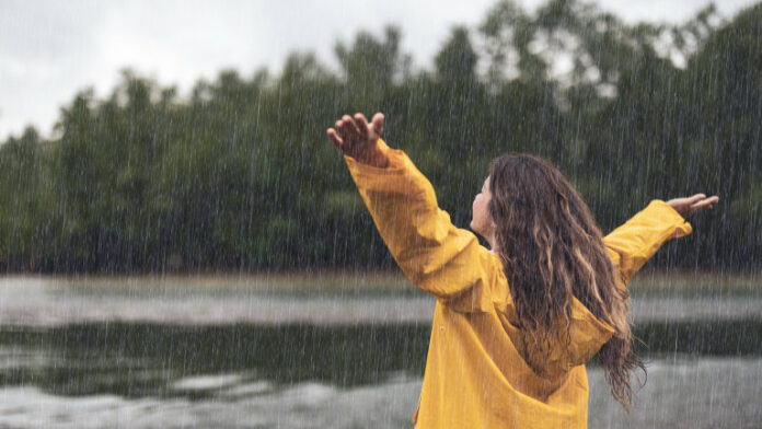 Back view of a carefree woman on rain by the river